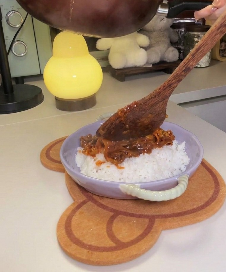 Inclinando la sartén para servir la mezcla espesa de ternera y kimchi sobre una base de arroz blanco en un bol lila.