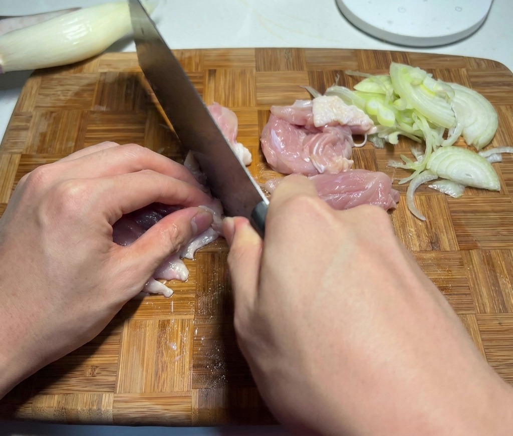 Un chef cortando carne cruda de contramuslo de pollo en trozos pequeños del tamaño de un bocado.