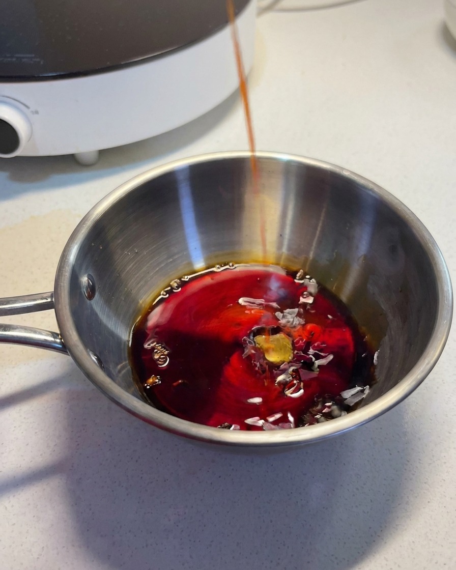 Un líquido oscuro y sabroso siendo vertido en un bol de acero inoxidable con otros ingredientes para la salsa.