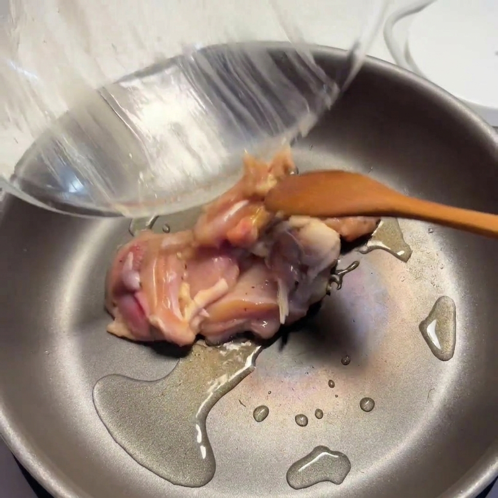 Trozos de pollo sazonados cocinándose en una sartén caliente con aceite, empezando a dorarse.