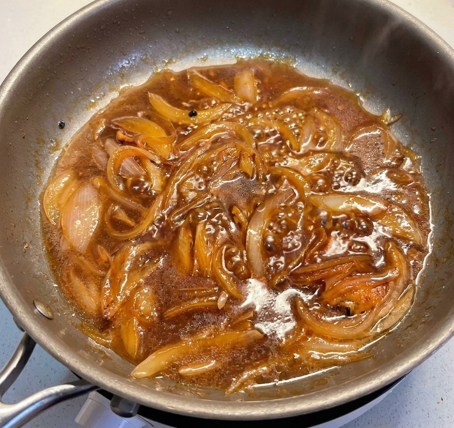 Rodajas de puerro verde añadiéndose a una salsa oscura burbujeante en una sartén de acero inoxidable.