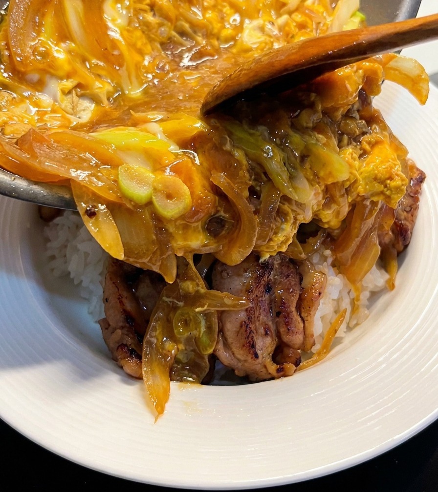 Una cuchara de madera ayudando a deslizar una mezcla brillante de huevos y cebolla sobre un bol de arroz con pollo.