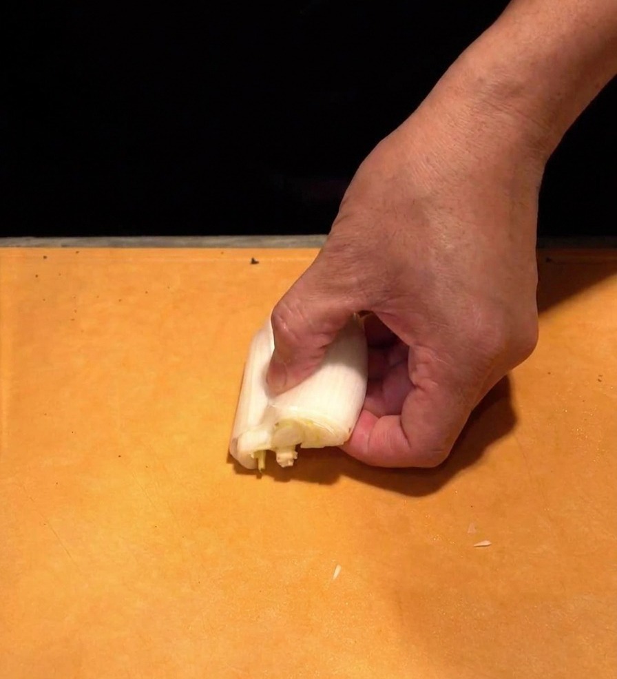 Una mano sujetando la parte blanca de una cebolleta naganegi y cortándola en tiras blancas muy finas.