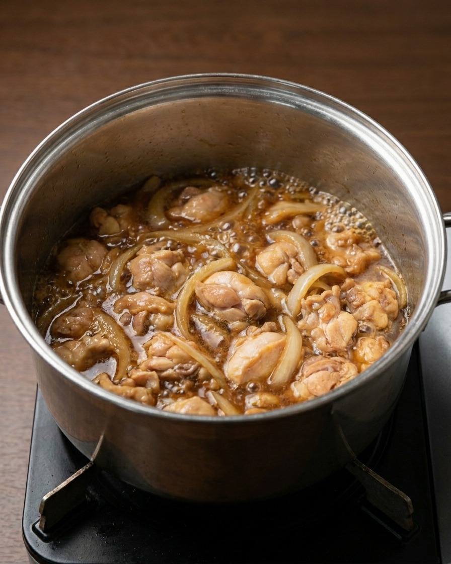 Una olla al fuego con trozos de pollo y cebolla hirviendo suavemente en un líquido oscuro y sabroso.