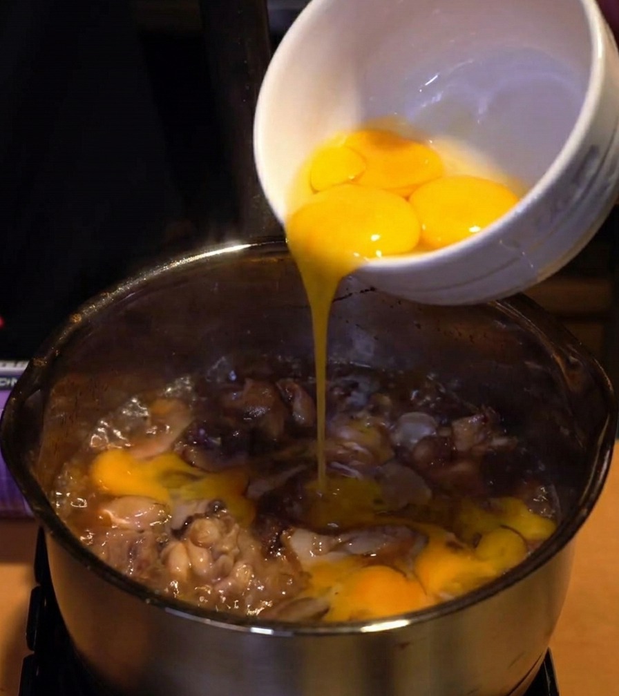 Claras de huevo batidas siendo vertidas desde un bol de cerámica blanca hacia la olla de pollo y cebolla.