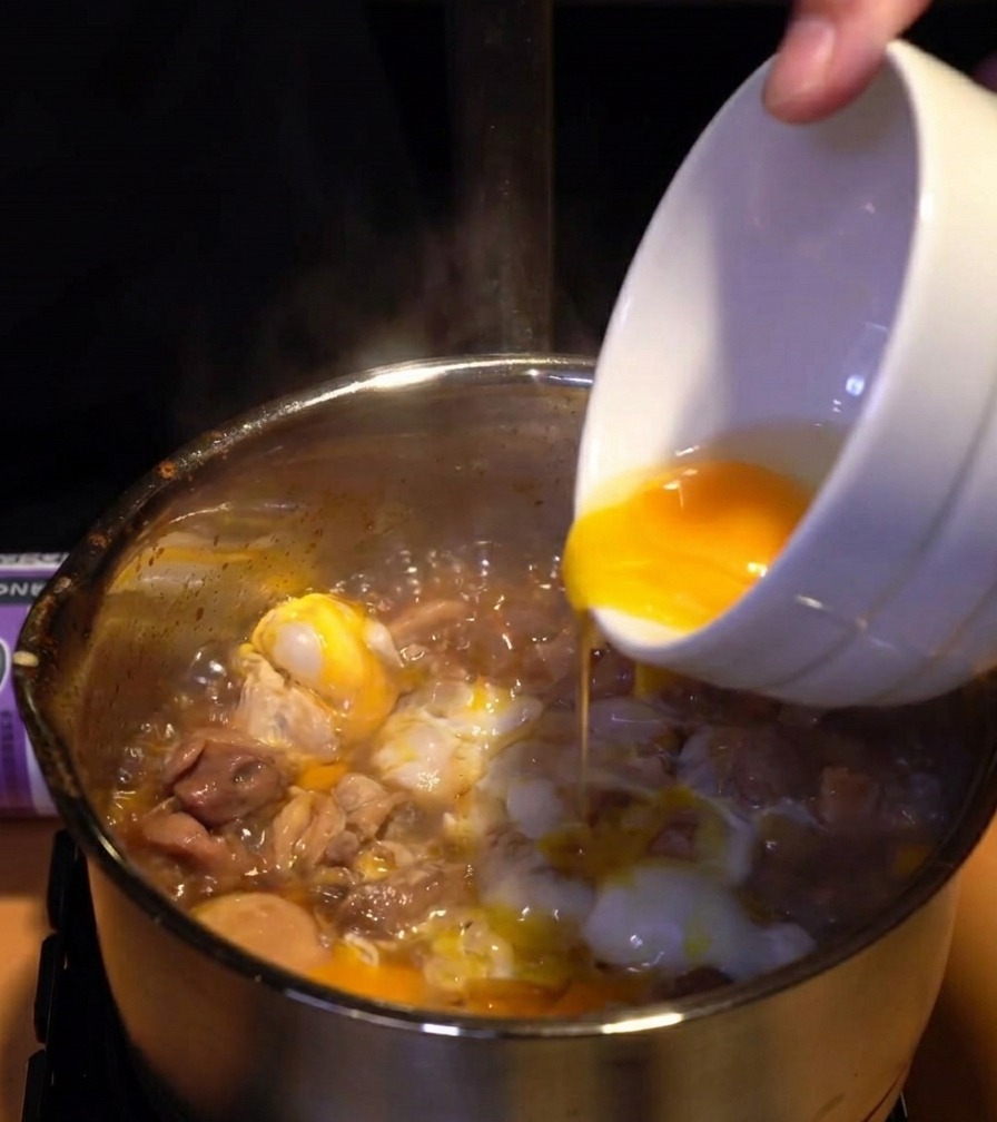 Yemas de huevo de color amarillo vibrante siendo vertidas sobre la capa de claras cocidas y pollo en la olla.