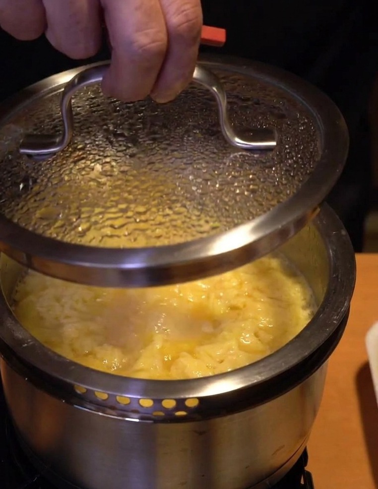 Primer plano de una mano colocando la tapa de cristal sobre la olla para dejar que el huevo termine de hacerse fuera del fuego.