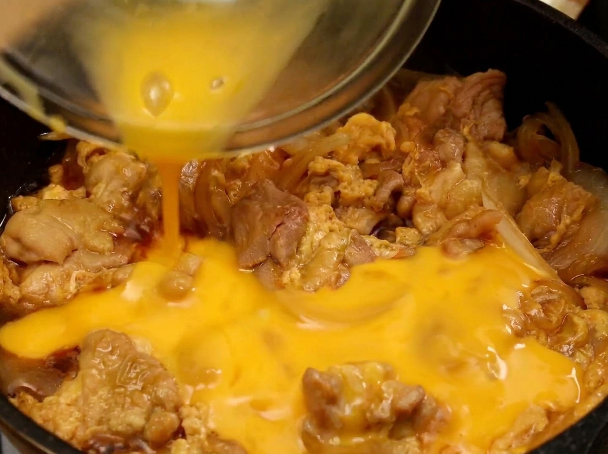 La parte final del huevo batido vertiéndose sobre el pollo y el huevo parcialmente cocinado en la sartén.
