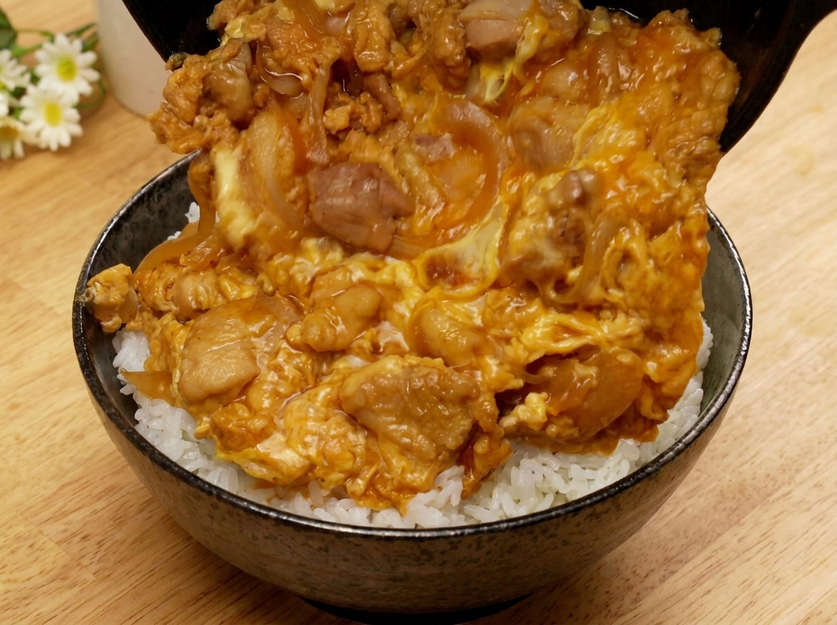 Inclinando la sartén para dejar que la mezcla de Oyakodon se deslice sobre un bol de arroz blanco.