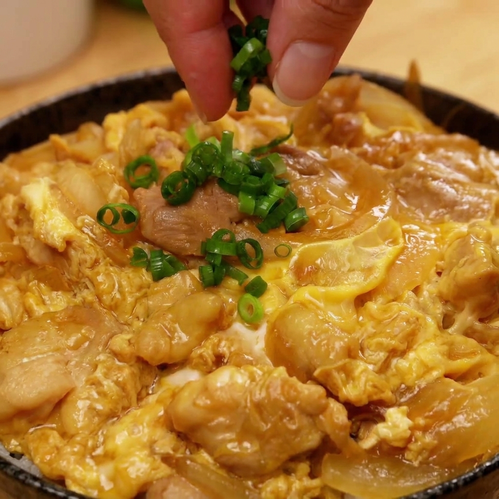 Una mano espolvoreando cebolleta picada sobre el centro de un bol terminado de Oyakodon.