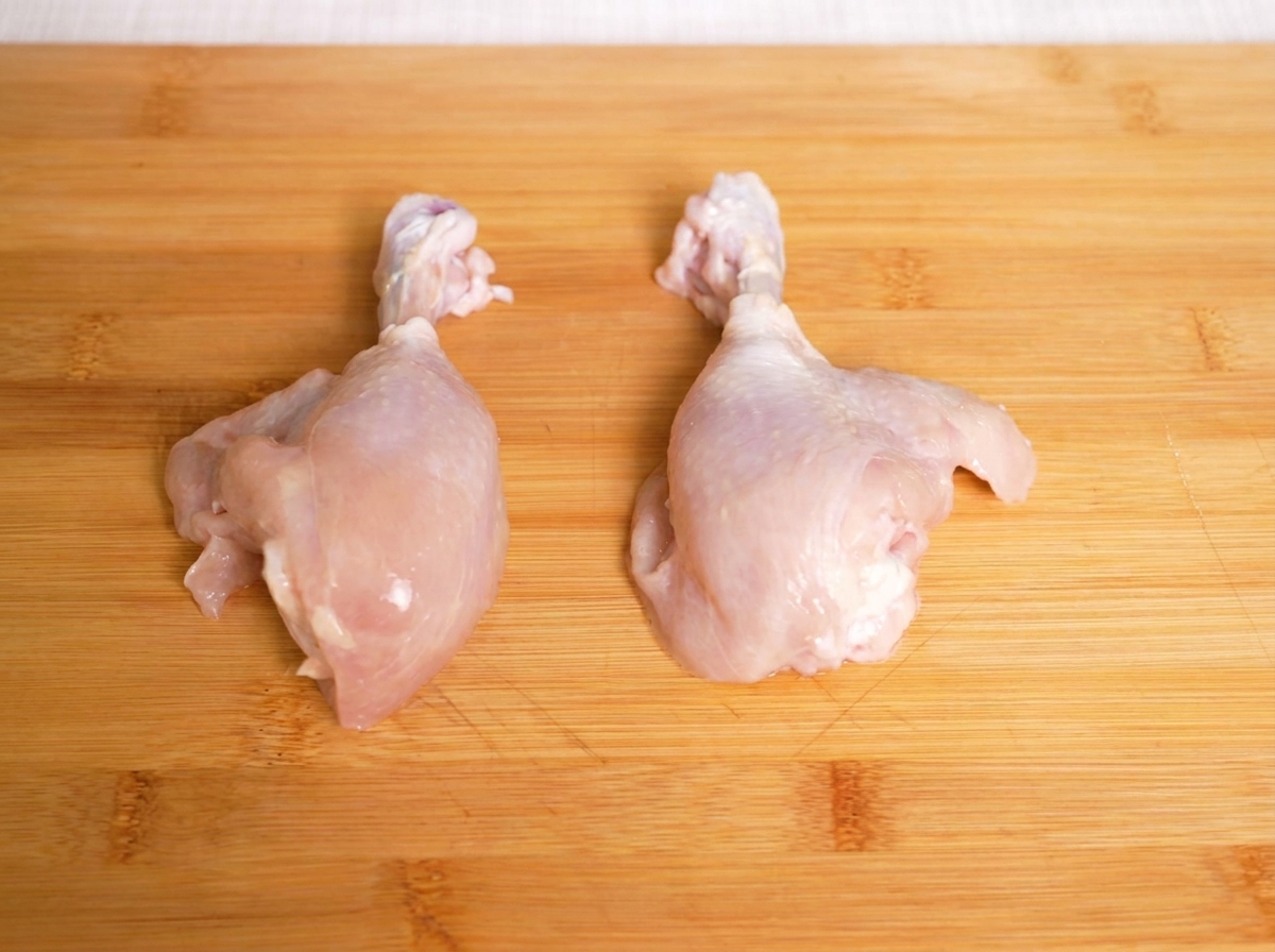 Contramuslos de pollo crudos sobre una tabla de cortar de madera, listos para ser troceados.