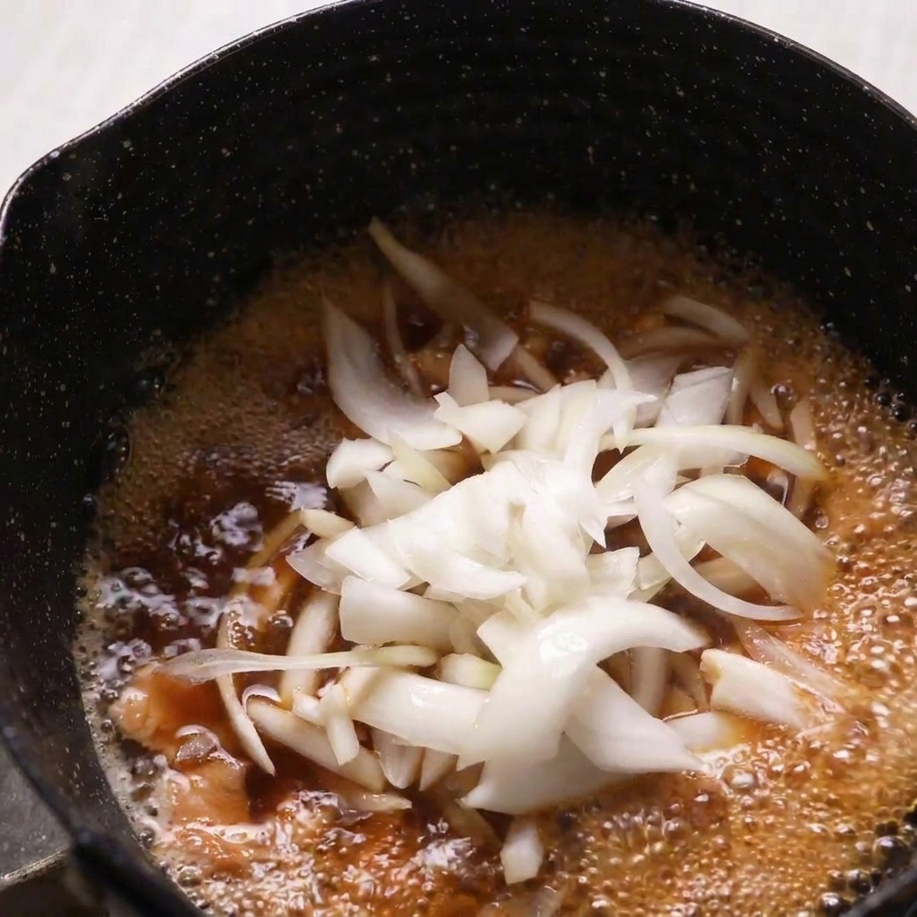 Cebollas cortadas finamente siendo añadidas a una sartén con pollo y caldo dashi hirviendo.