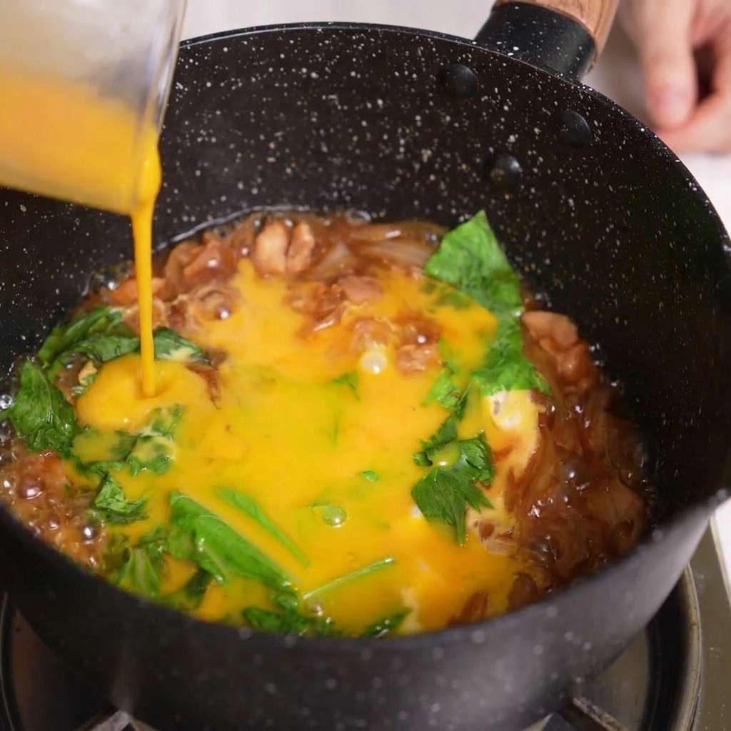 Vertiendo la última parte del huevo batido desde una jarra sobre los ingredientes del Oyakodon.