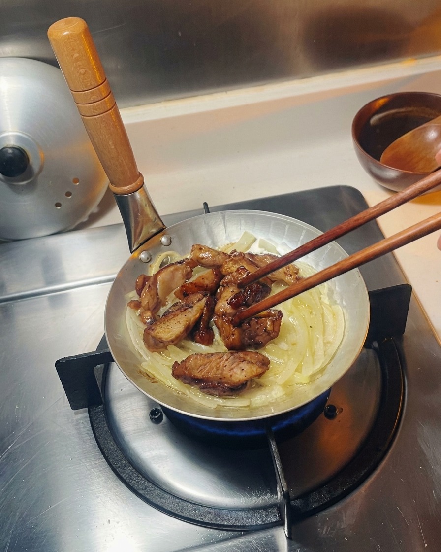 Trozos de pollo frito colocándose sobre una cama de cebollas salteadas translúcidas en una pequeña sartén de cocción plateada.