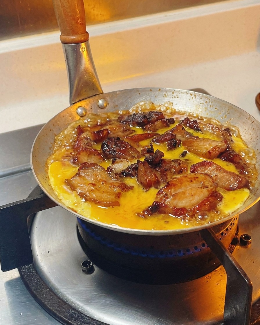 Mezcla de huevo batido vertiéndose con movimientos circulares sobre pollo y cebollas hirviendo a fuego lento en una salsa.