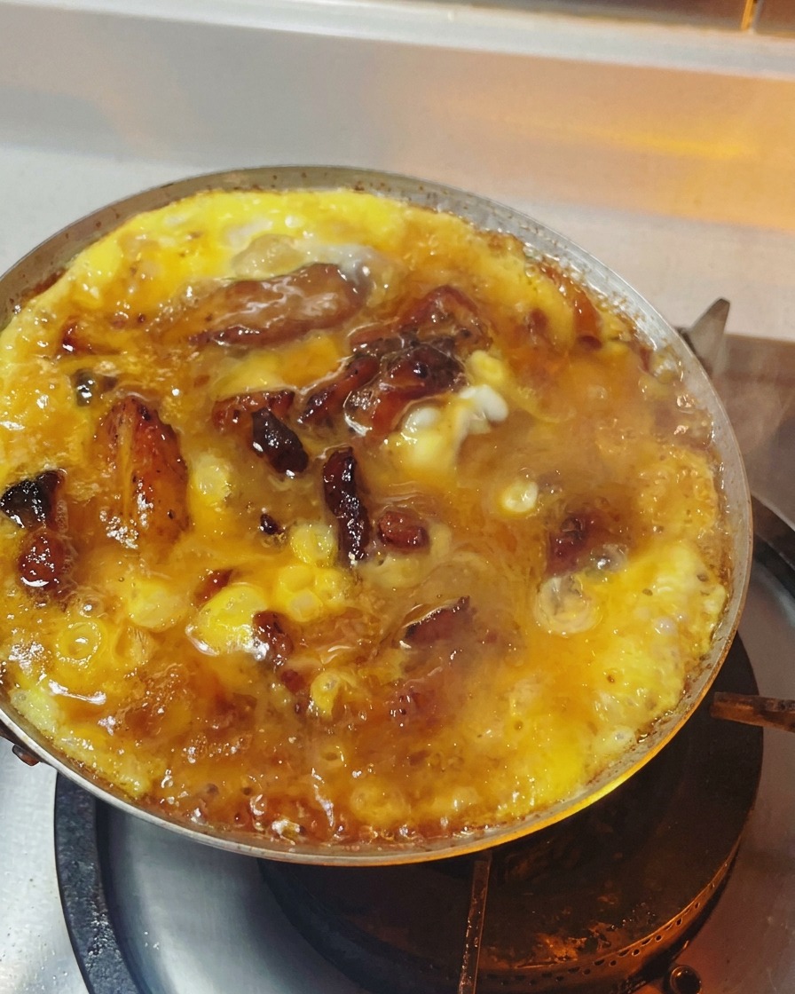 Oyakodon en una sartén con los huevos cocinados a una textura suave, semisólida y brillante sobre una cama de pollo y cebollas.