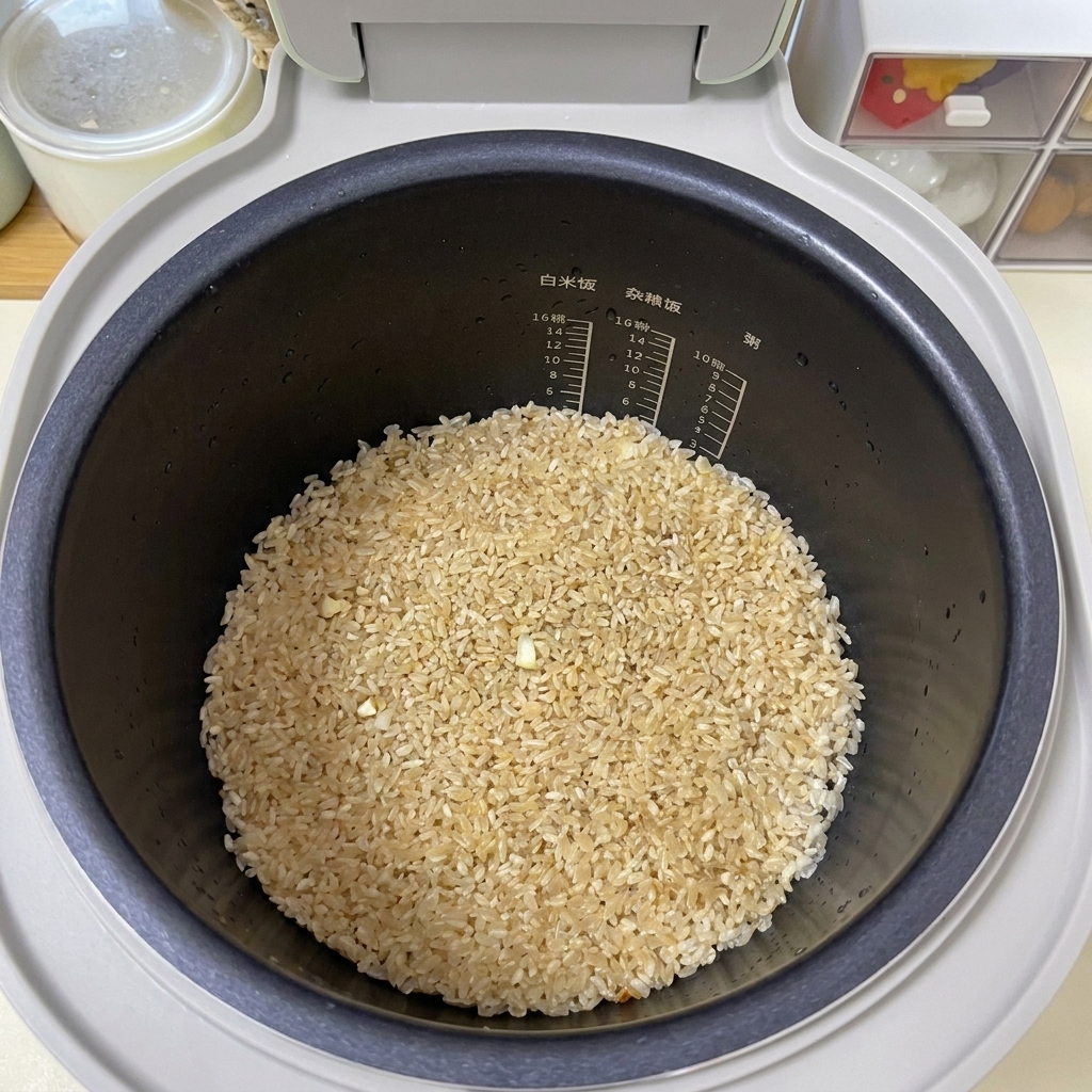 Arroz sazonado de color marrón claro aplanado uniformemente en el fondo de una olla arrocera negra.