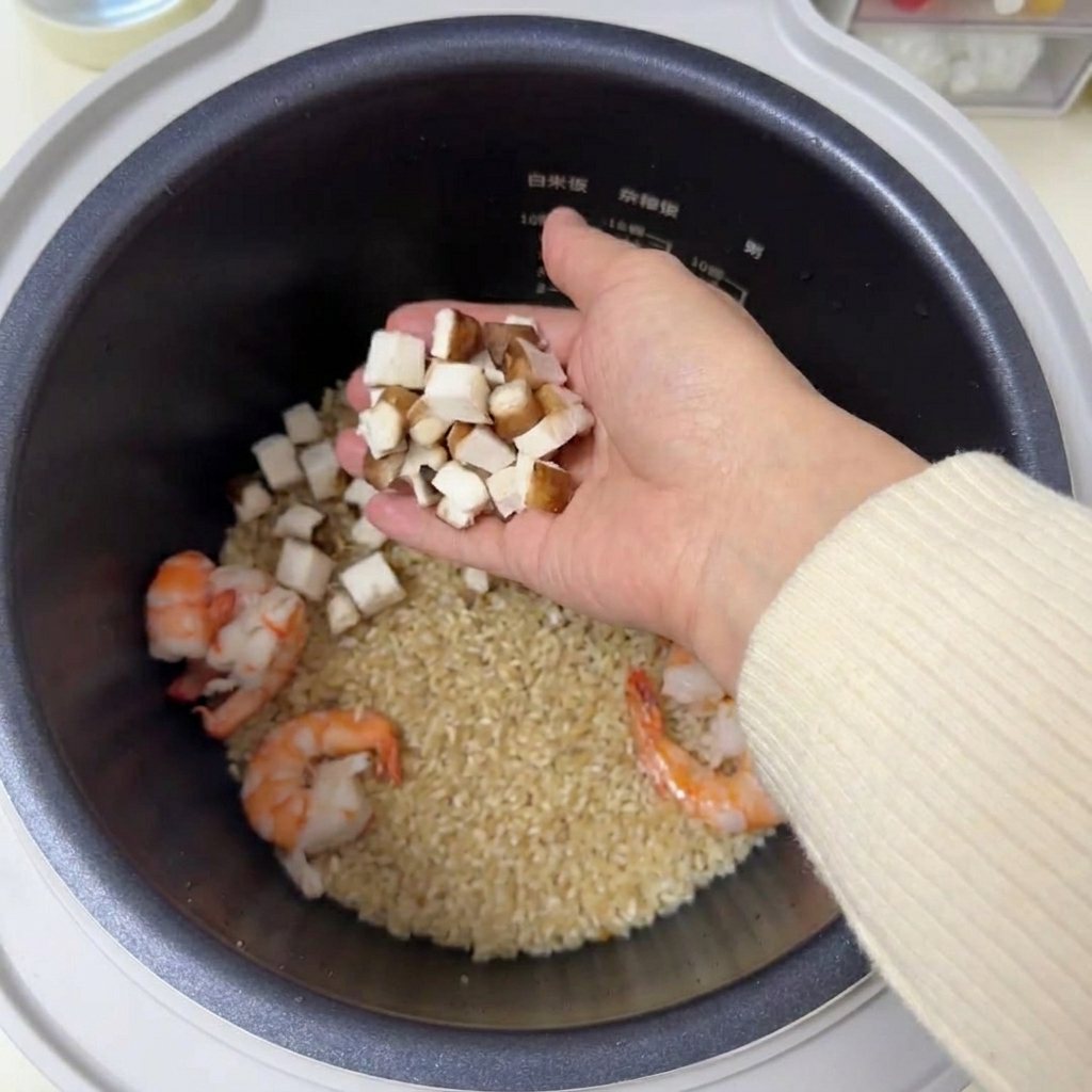 Trocitos de champiñones shiitake marrones en una mano sobre una arrocera con arroz y camarones.