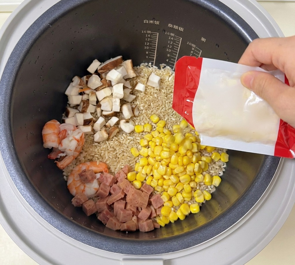 Granos de maíz dulce cayendo desde un paquete a la olla arrocera con arroz, camarones y vegetales.