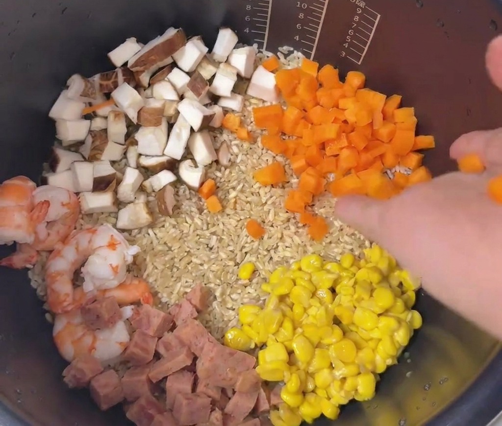 Arreglo colorido de zanahorias, maíz, jamón, champiñones y camarones sobre el arroz en la olla.