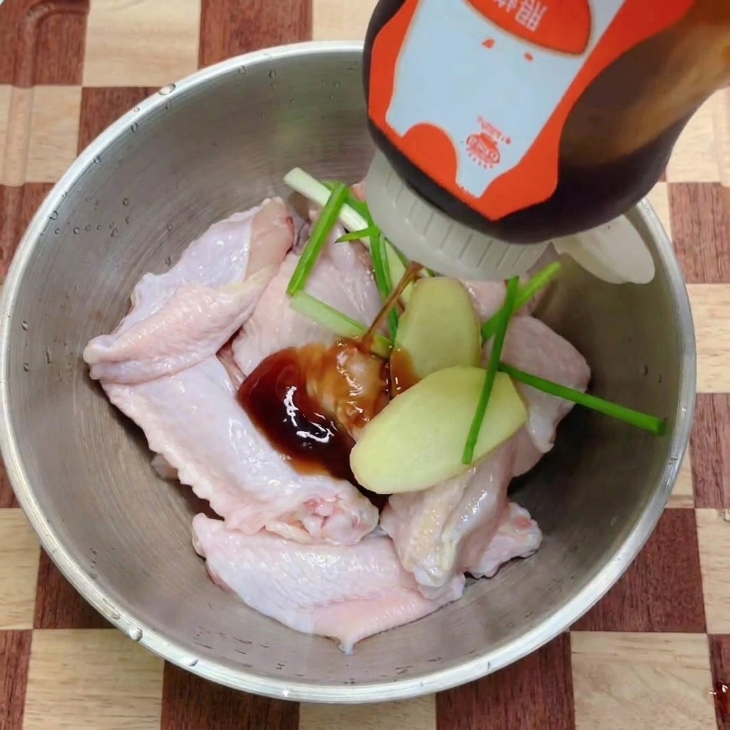 Salsa teriyaki oscura vertiéndose sobre un bol de alitas de pollo crudas decoradas con hierbas aromáticas frescas.