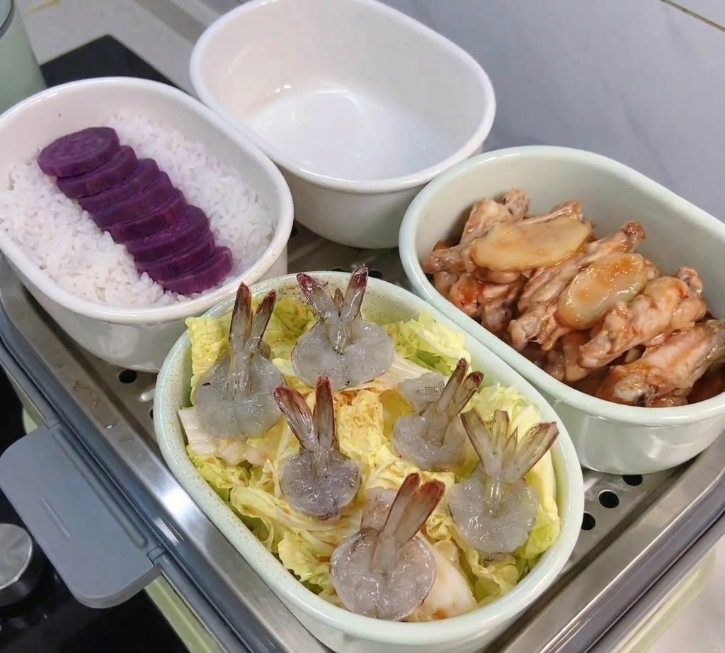 Un plato ovalado blanco con capas de hojas de repollo baby cubiertas con varios camarones crudos pelados, listo para la vaporera.