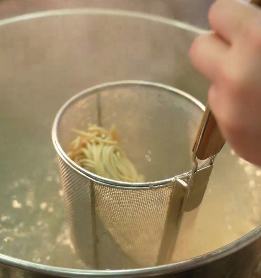 Un colador con fideos ramen sumergido en una olla profunda con agua hirviendo.