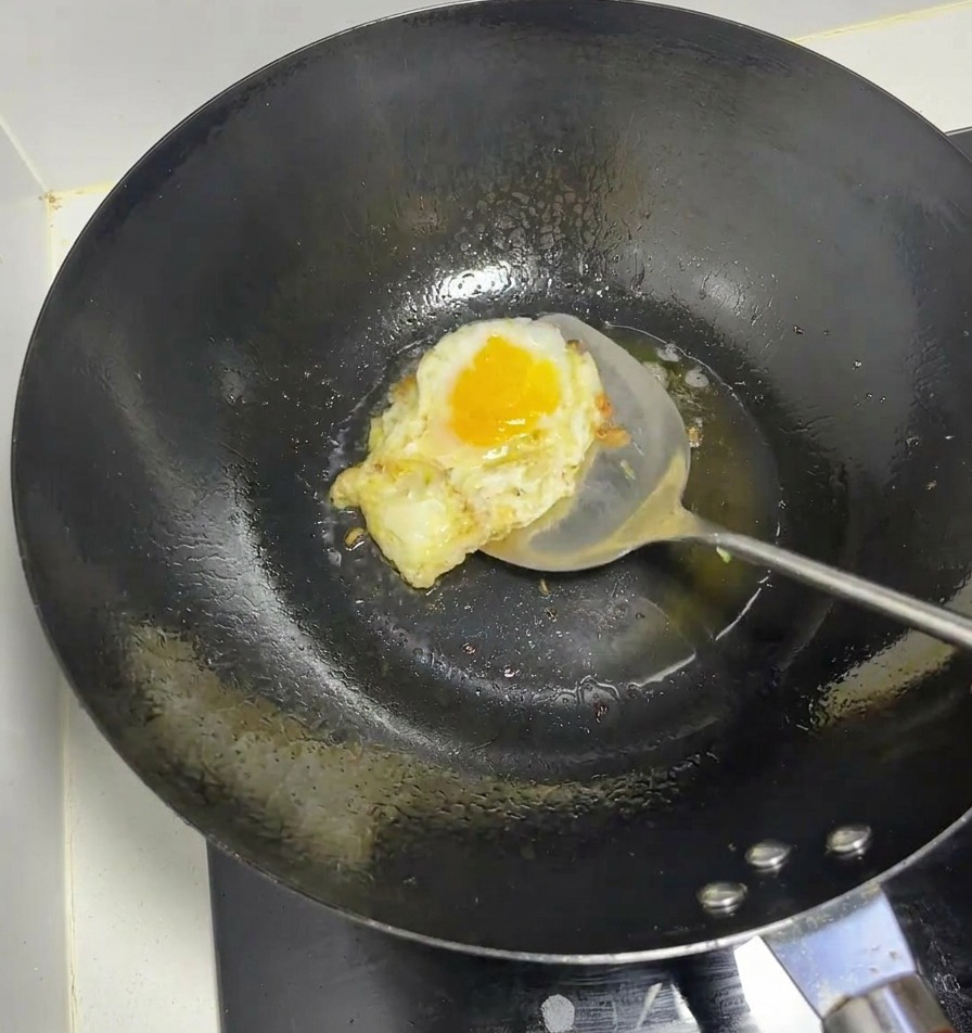 Un huevo friéndose en un wok caliente con una espátula de metal.