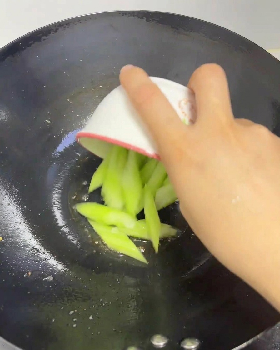 Rodajas de lufa fresca de color verde cayendo desde un tazón pequeño a un wok caliente.
