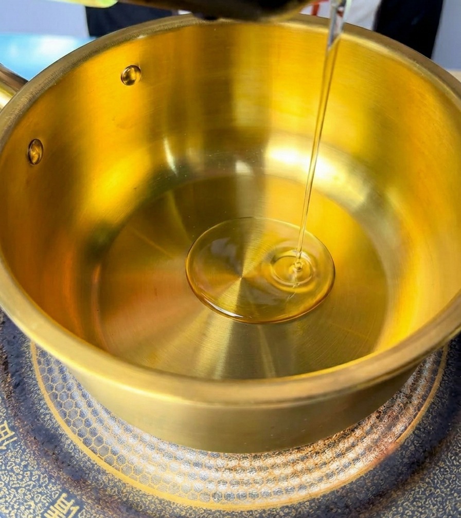 Aceite vertiéndose en una olla de latón dorada sobre una placa de inducción.