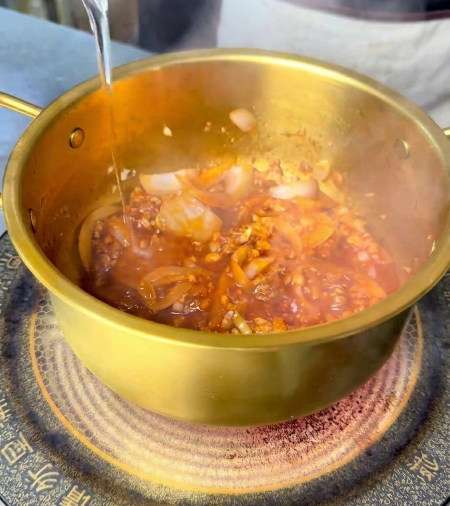 Agua vertiéndose en la olla para mezclarse con la base picante de carne y salsa.