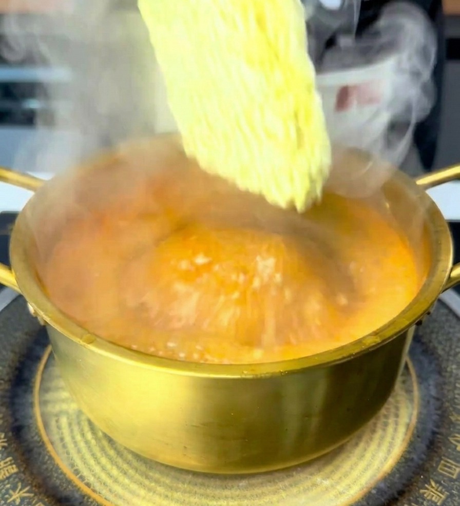 Colocando el bloque de fideos ramen secos en el caldo rojo hirviendo dentro de la olla.
