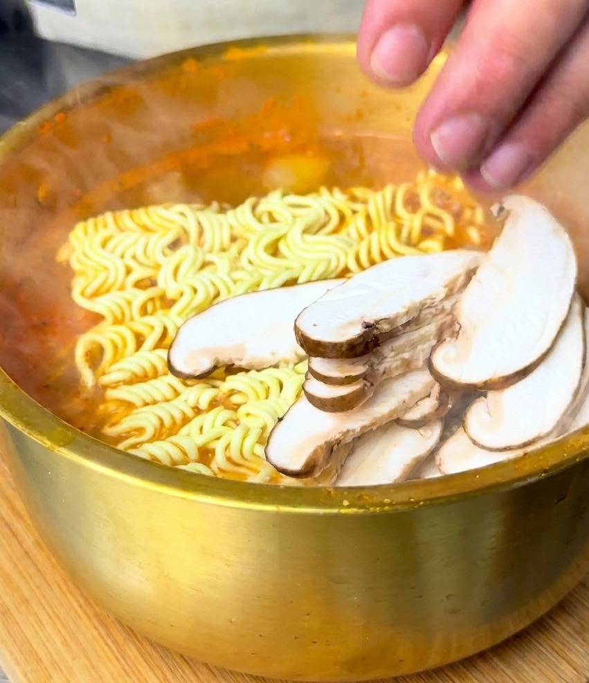 Setas shiitake en rodajas colocadas sobre los fideos en el caldo picante.