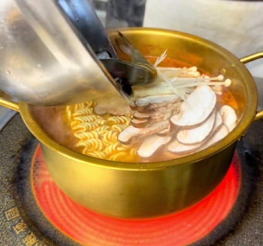 Camarones y mejillones frescos añadiéndose a la olla hirviendo con fideos y setas.
