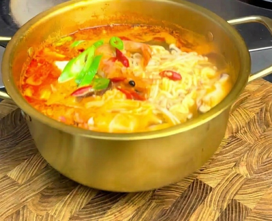 Ramen de mariscos en la olla dorada con rodajas de chile fresco sobre una tabla de madera.