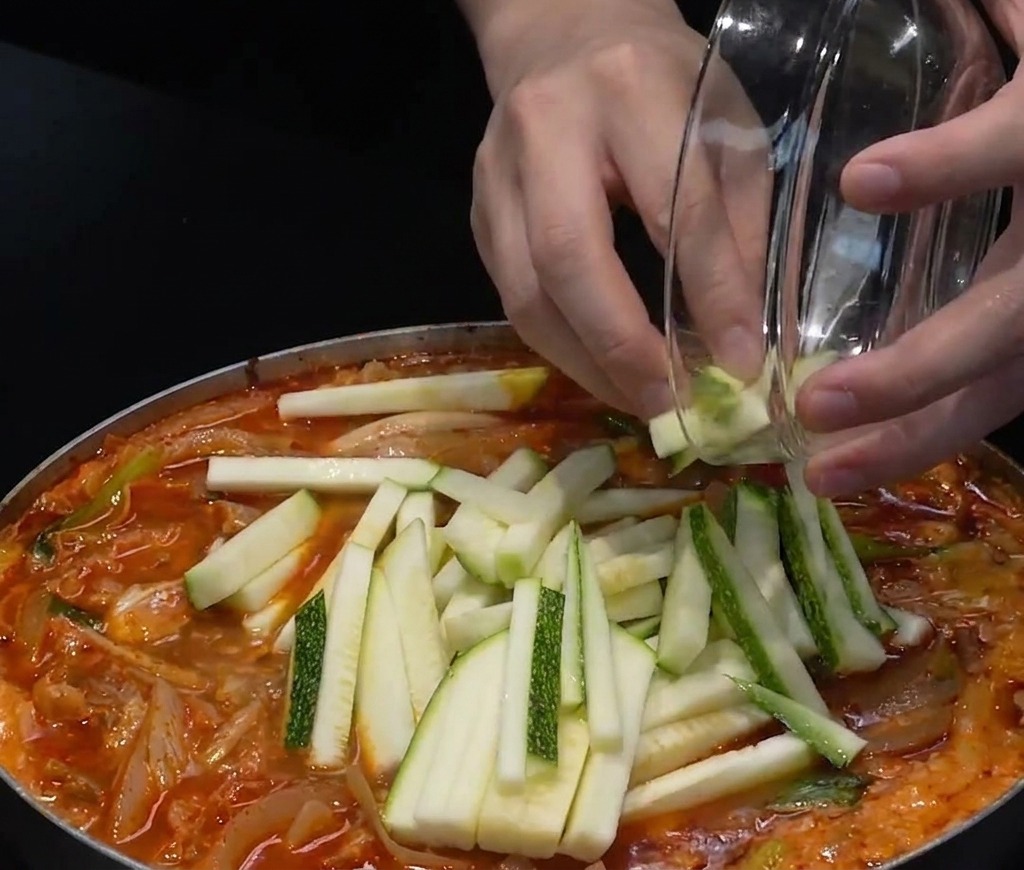 Rodajas de calabacín y chiles verdes picados añadiéndose a la superficie de la sopa de mariscos.