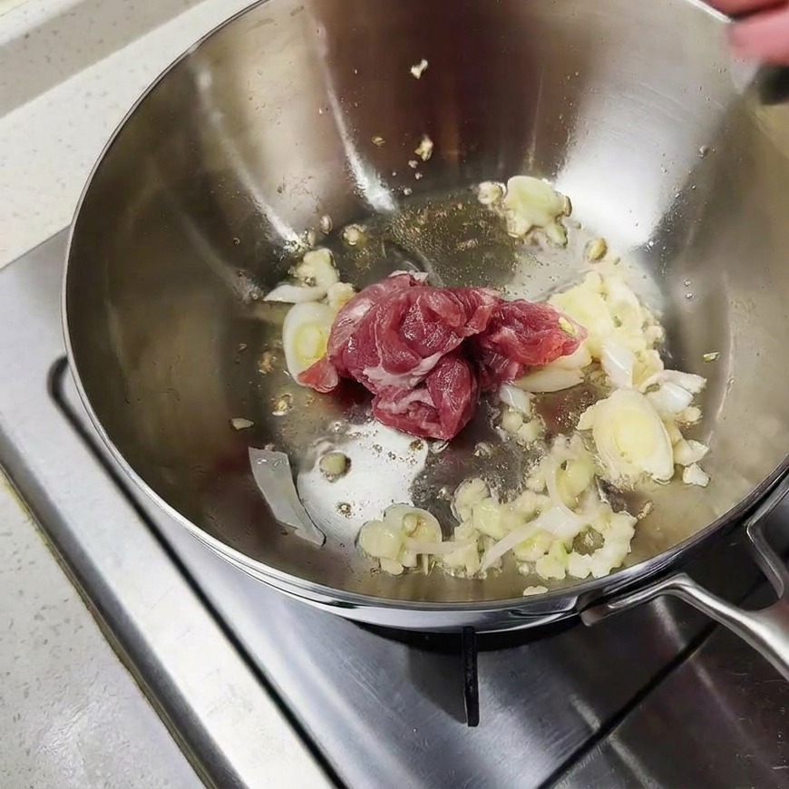 Trozos de cerdo crudo salteándose con aromáticos en el fondo de una olla metálica.