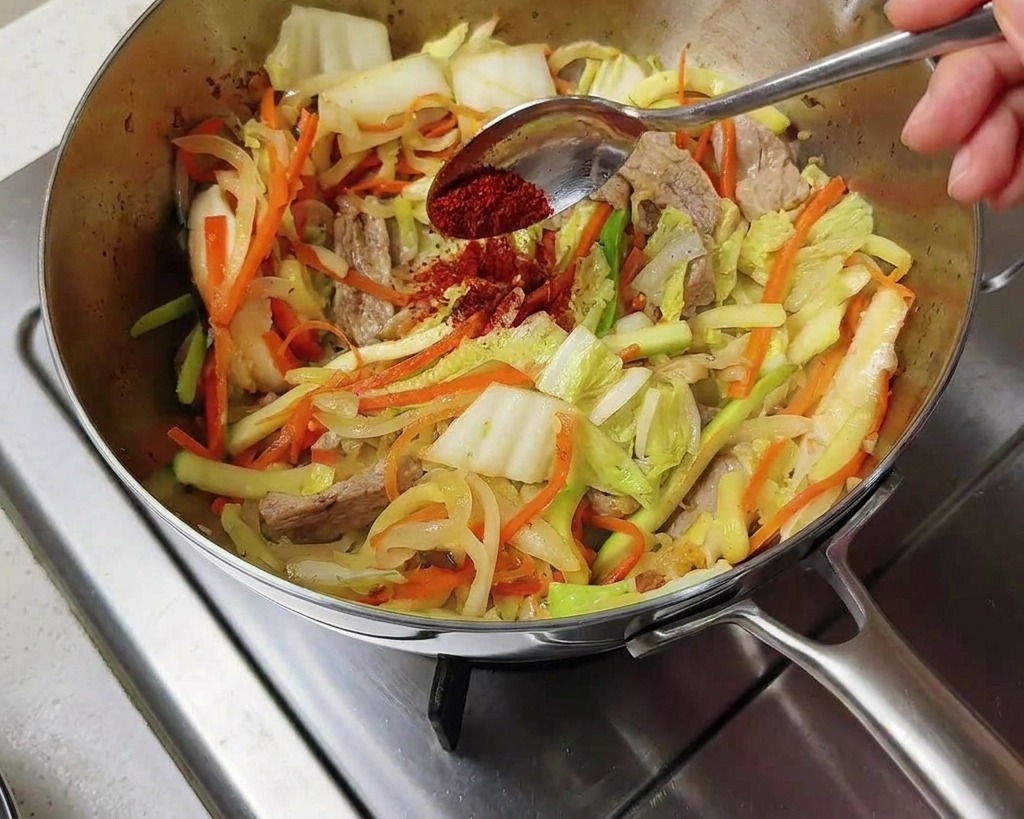 Chile coreano rojo vibrante en polvo espolvoreándose desde una cuchara sobre las verduras salteadas.
