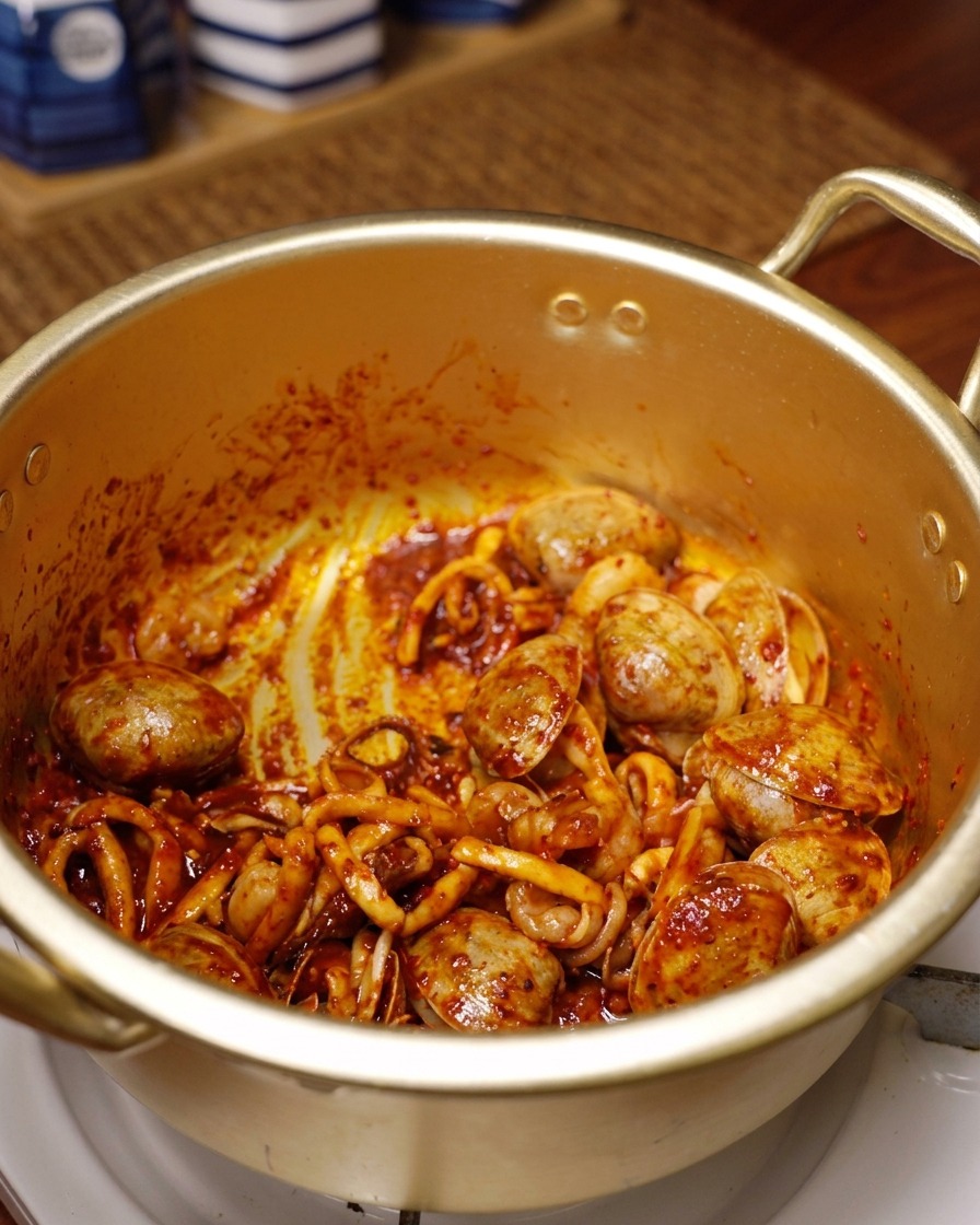 Calamares, langostinos y almejas cubiertos de chile rojo vibrante salteándose en una olla dorada.