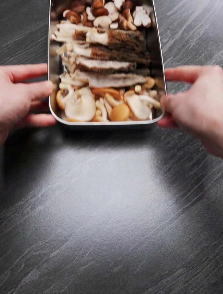 Manos sosteniendo una bandeja con colmenillas laminadas y setas shiitake cortadas por la mitad.