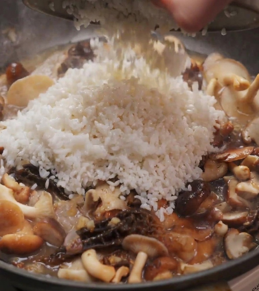 Arroz blanco vertiéndose desde un cuenco a una sartén con setas shiitake y colmenillas salteadas.