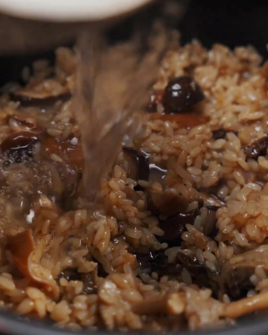 Agua vertiéndose en una olla que contiene la mezcla sazonada de arroz y setas.