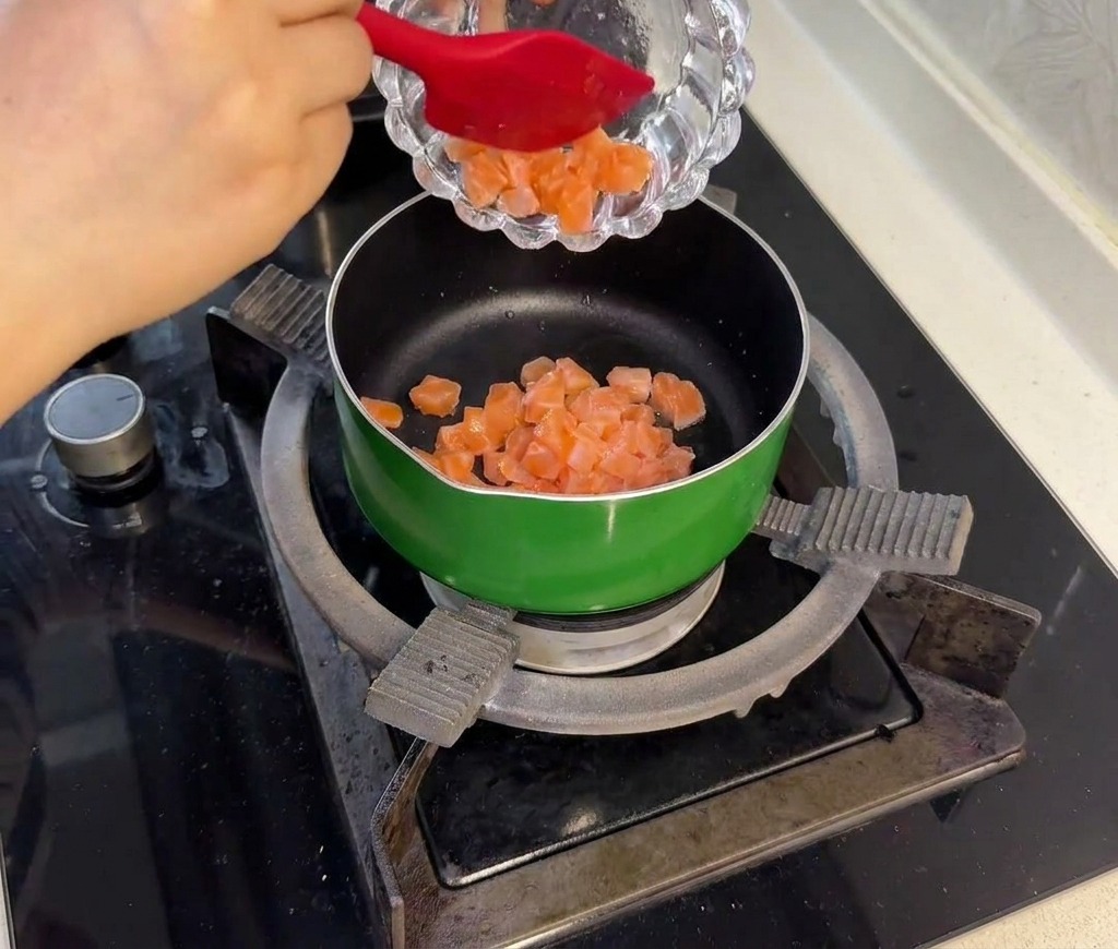 Cubos de salmón crudo marinados siendo salteados en una sartén verde hasta que el exterior se vuelve opaco.