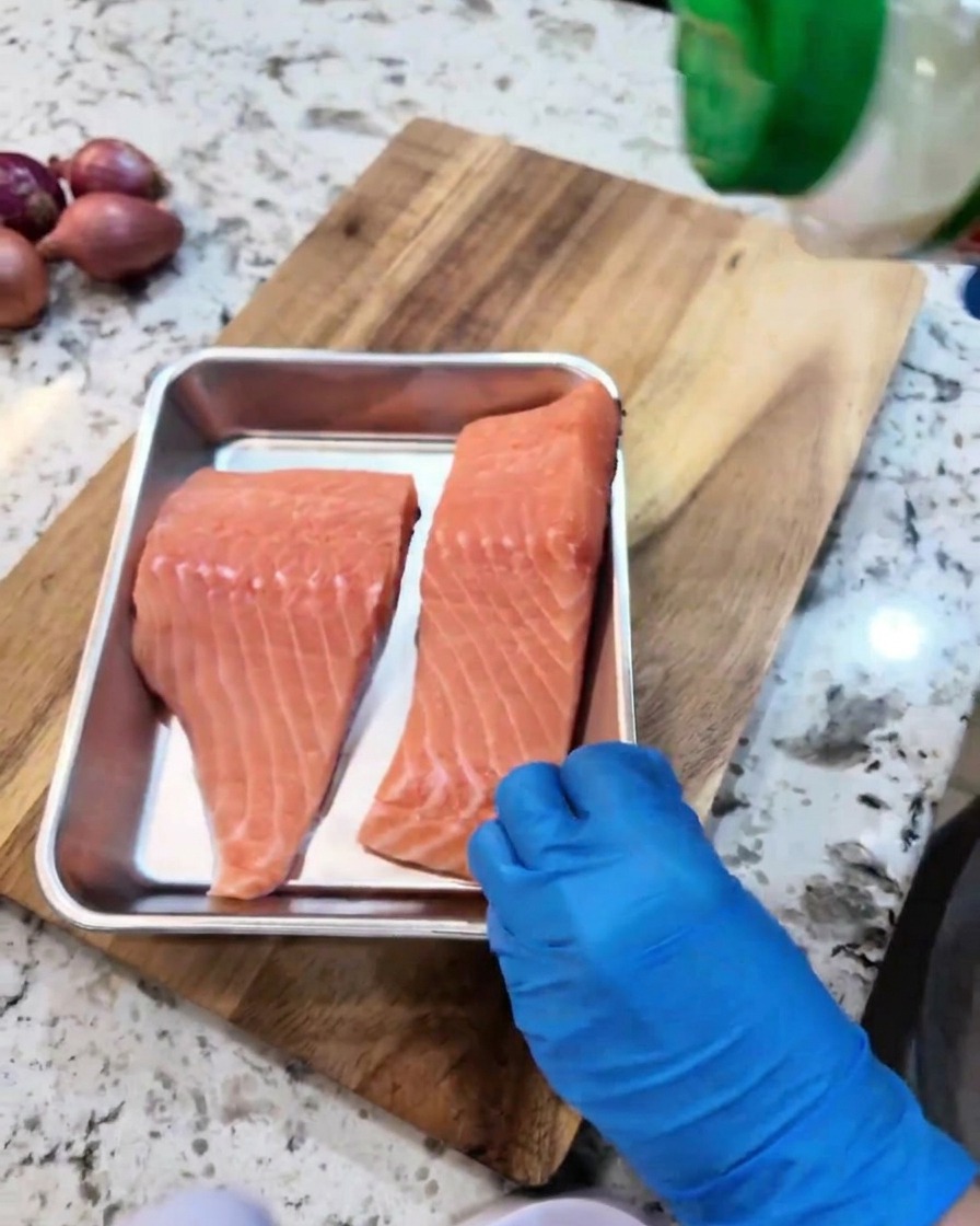 Filetes de salmón crudos sazonados con ajo en polvo y pimienta negra en una bandeja de metal.