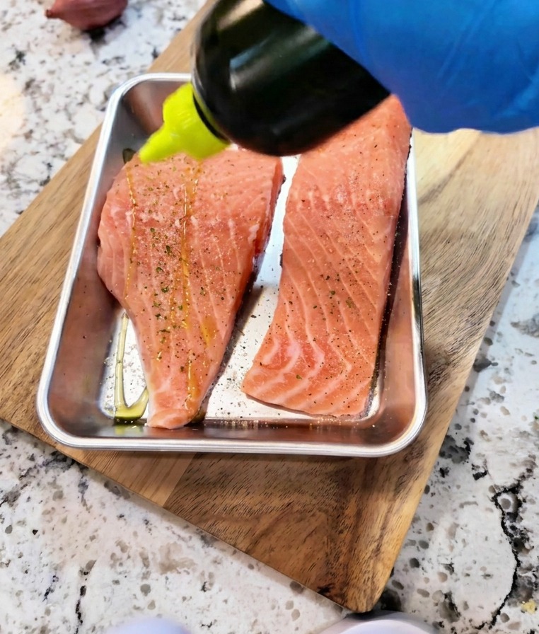 Salsa de soja y aceite vertiéndose sobre filetes de salmón sazonados para marinar.