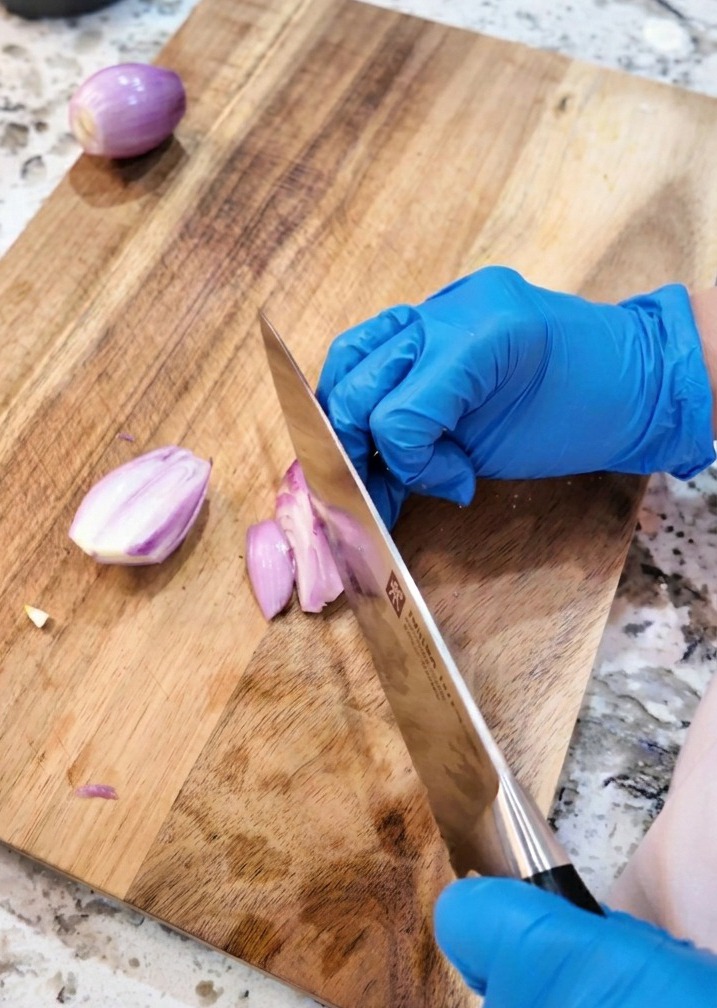 Un cuchillo de cocina cortando chalotas moradas en rodajas finas sobre una tabla de madera.