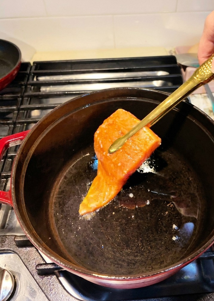 Filetes de salmón marinados colocándose en una olla de hierro fundido caliente con pinzas de cocina.