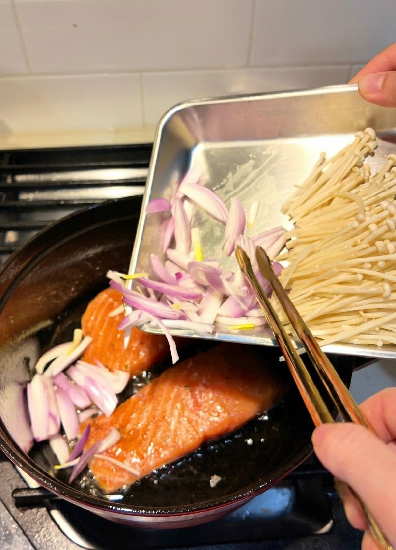 Chalotas cortadas añadiéndose a una olla donde los filetes de salmón se están sellando.