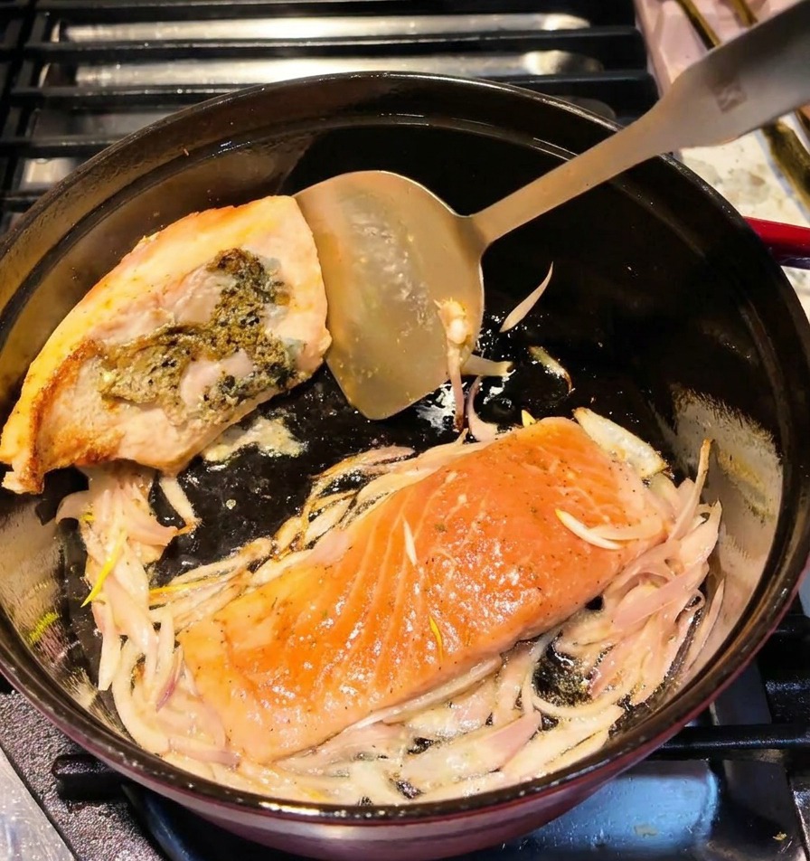 Una espátula metálica dando la vuelta a un filete de salmón en una olla, mostrando una superficie dorada.