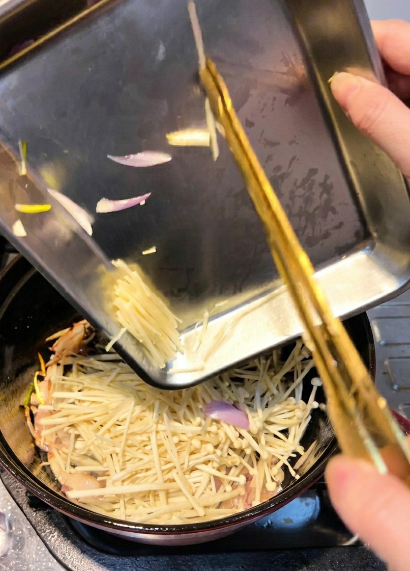 Setas enoki añadiéndose a una olla para ser salteadas con las chalotas sofritas.